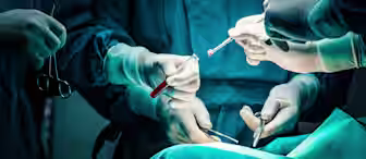 A group of surgeons wearing gloves and surgical gowns performing a surgery. Multiple hands hold various surgical instruments under bright operating lights. The scene is focused on the surgical area, displaying precise coordination and teamwork.