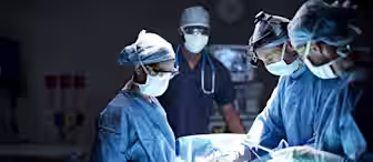 A surgical team, comprising three surgeons and one assisting nurse in blue scrubs and masks, performing an operation in a well-lit operating room. Medical equipment is visible in the background, and the team is intently focused on the procedure.