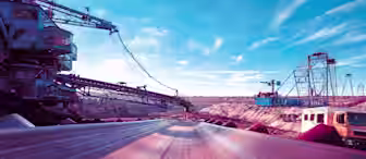 A conveyor belt runs through an open-pit mining site under a bright blue sky. Heavy machinery and cranes can be seen on either side, and rugged, rocky terrain stretches into the distance. A truck is parked to the right, emphasizing the scale of the operation.