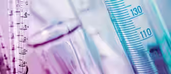Close-up of various measurement instruments used in a laboratory setting. The image features clear cylindrical tubes marked with measurement scales in milliliters. The colors are predominantly shades of blue and pink, giving the scene a vibrant hue.