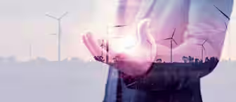 A double exposure image showing a person in a suit with an extended hand, overlaid with wind turbines in the background. The person appears to be holding a bright light, symbolizing renewable energy and sustainability.