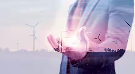 A double exposure image showing a person in a suit with an extended hand, overlaid with wind turbines in the background. The person appears to be holding a bright light, symbolizing renewable energy and sustainability.