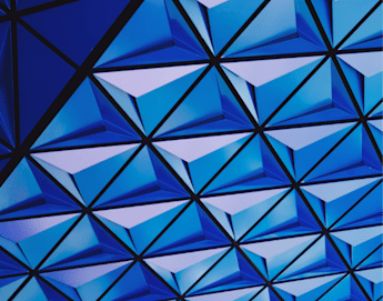 The image shows a complex geometric pattern of interconnected, blue triangular facets. The design creates a futuristic and symmetrical 3D effect, with varying shades of blue contributing to an overall sense of depth and movement.