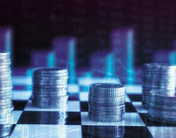 Stacks of coins are arranged in rows on a black and white checkered surface. In the background, blurred bar charts and line graphs are visible, creating a financial or economic theme. The image is filled with blue and purple hues, giving it a futuristic feel.