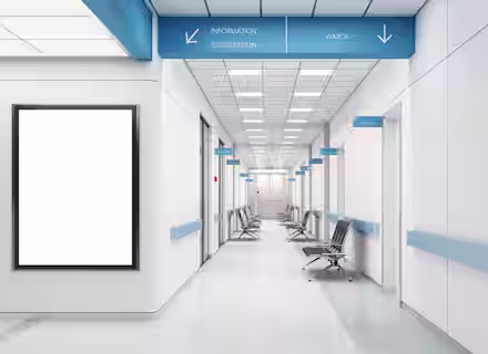 Modern hospital corridor with white walls, blue accents, empty chairs, and signs for information, registration, wards, and CT room. A large blank notice board is on the left wall. The area is clean and brightly lit.