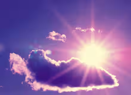A brilliant sun shines behind a fluffy cloud in a purple and blue sky. Sun rays radiate outward, casting a warm glow around the cloud. A hint of lens flare adds an ethereal touch to the vibrant scene.