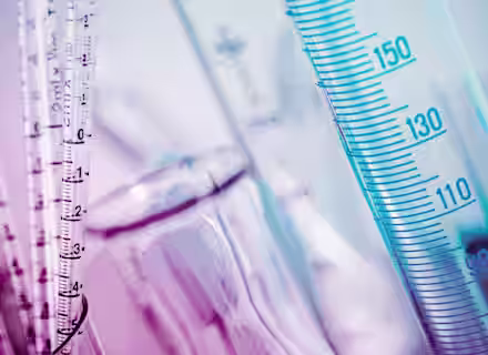 Close-up of various measurement instruments used in a laboratory setting. The image features clear cylindrical tubes marked with measurement scales in milliliters. The colors are predominantly shades of blue and pink, giving the scene a vibrant hue.