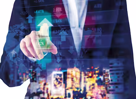 A person in a suit touches a virtual screen with financial data, including charts and stock market indices, overlaid on a global map. The background displays a blurred cityscape at night, highlighting the dynamic nature of global finance.