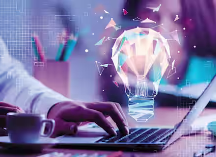A person types on a laptop with a cup of coffee nearby. A digitally rendered, glowing light bulb made of geometric shapes floats above the laptop, symbolizing an idea or innovation. The background includes a pencil holder and blurred figures.