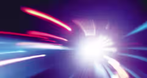 An abstract image depicting vibrant light streaks radiating outward from a bright center, creating a dynamic sense of motion. The colors predominantly feature shades of blue, pink, and purple against a dark background, enhancing the overall glowing effect.