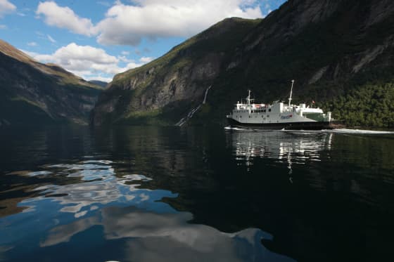 Ferry on a calm fjord between steep mountains.