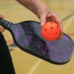 A person holding and pickleball paddle and ball 