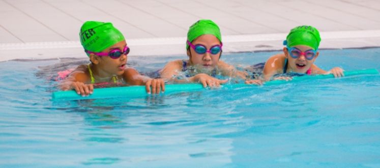 girls in green hats swimming with pool noodle
