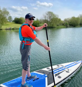 smiling man with navy hat and sunglasses on paddleboard on Stanborough Lake