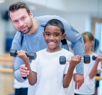 Junior fitness class - instructor with boy lifting hand weights
