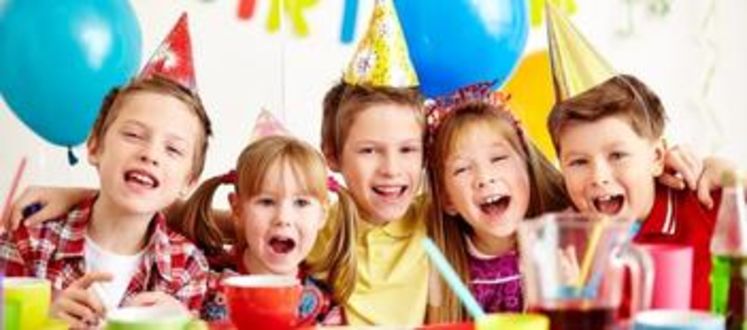 Image shows a group of children with party hats on enjoying party food. 