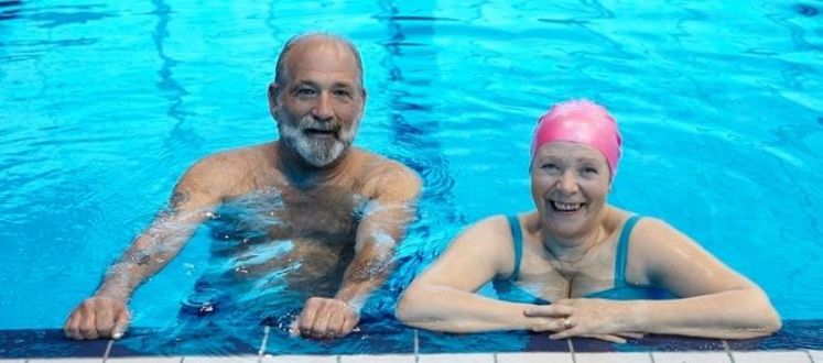 senior male and female leaning on the pool wall smiling in a swimming pool
