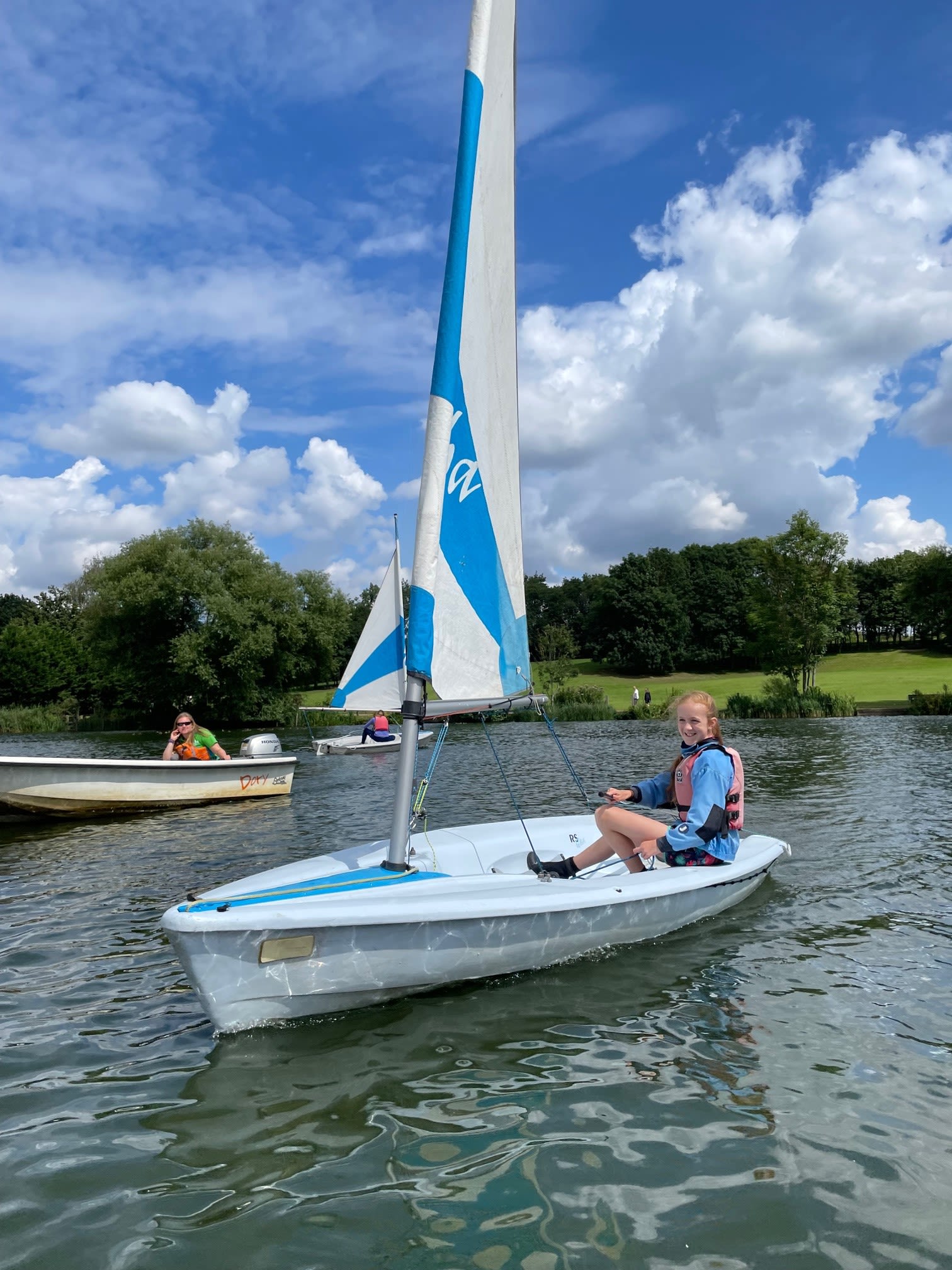 Young girl sailing dinghy on Stanborough Lake large white and blue sail