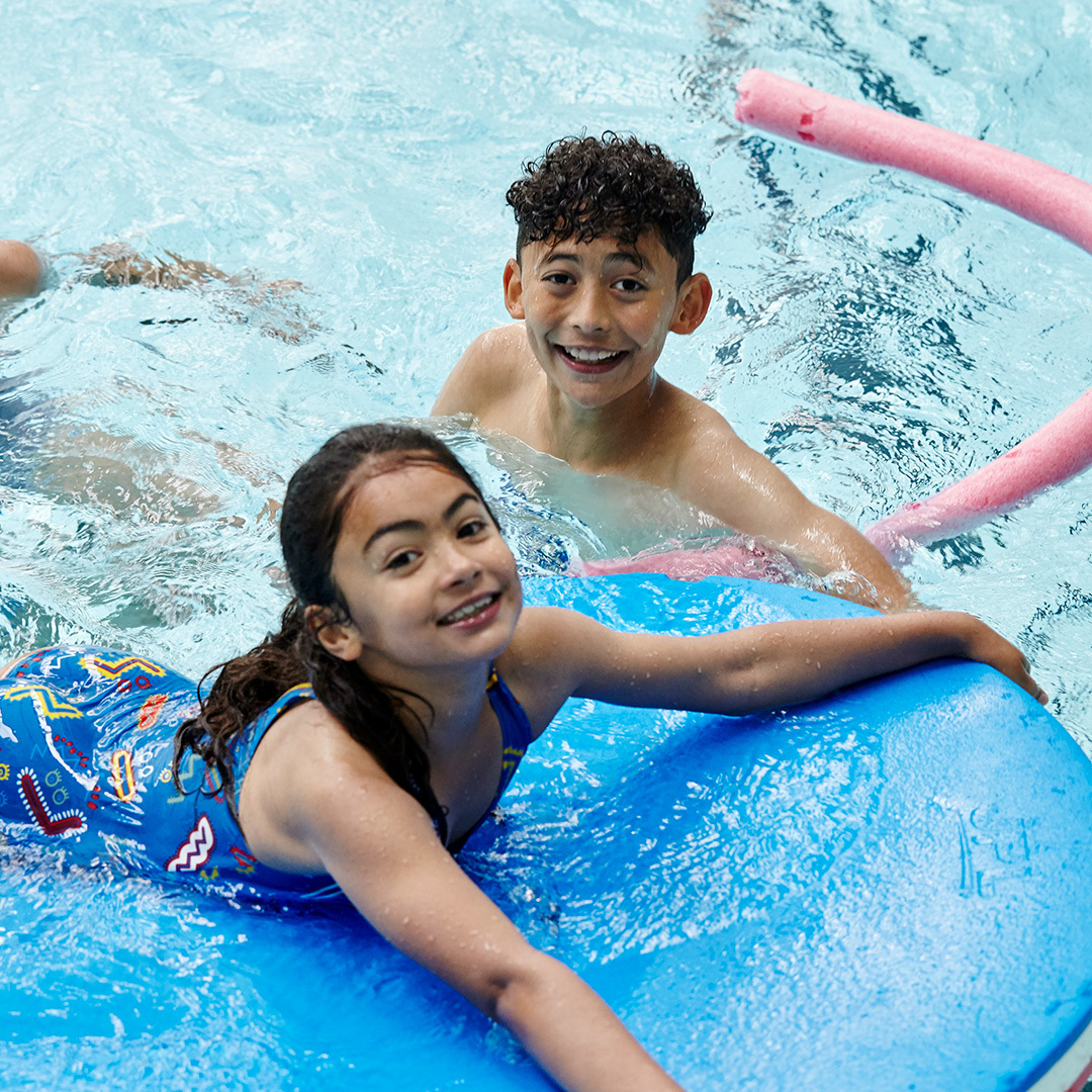 image shows two teenagers in a swimming pool with a float.  They are both smiling.