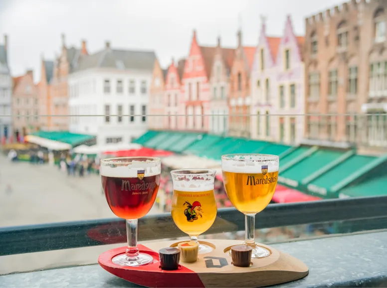 A Row of Belgian Beer in Glasses in Front of a Window Overlooking Gabled Houses