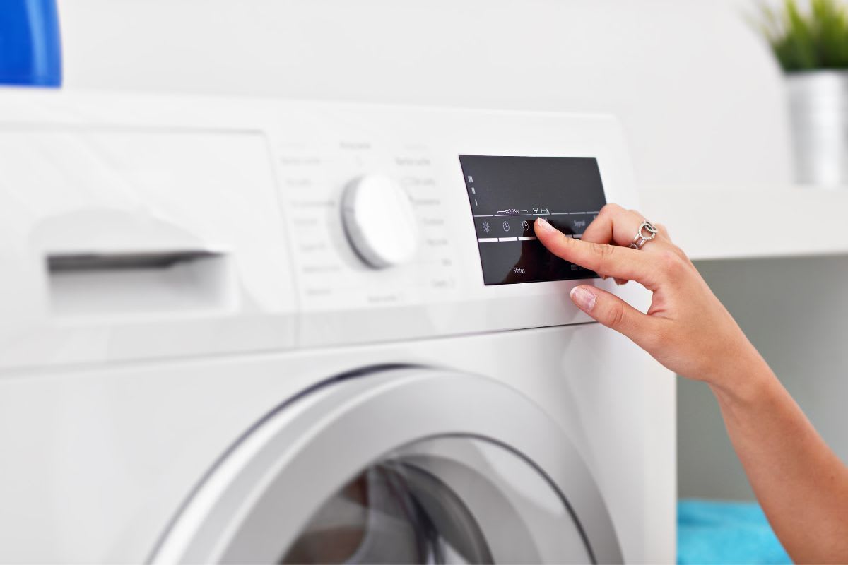 Hand berührt das digitale Bedienfeld einer modernen Waschmaschine.