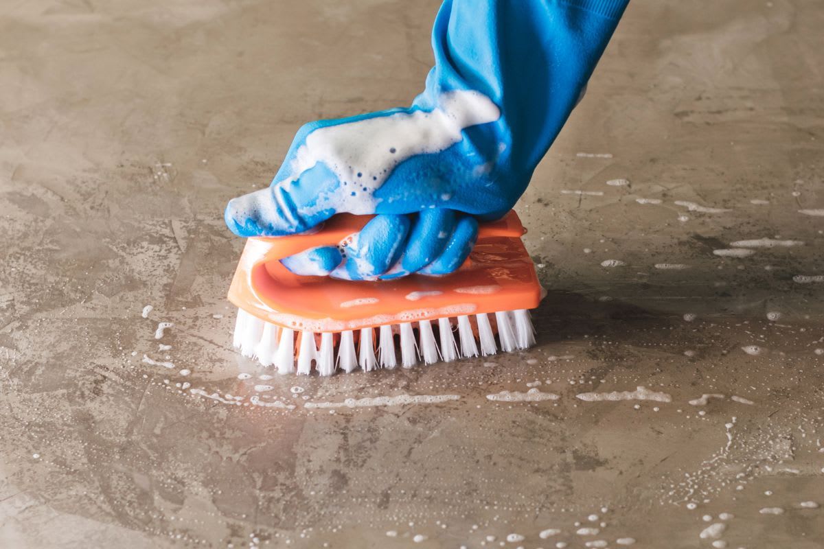 Person reinigt Betonterrassenplatten mit Bürste und Seifenlauge, ein Beispiel für die einfache und effektive Reinigung mit Hausmitteln.