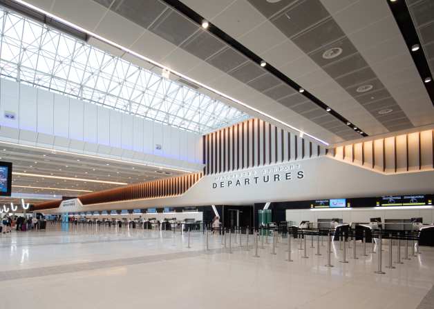 Modern airport departures hall with a long, angular counter and a large "MANCHESTER AIRPORT DEPARTURES" sign.