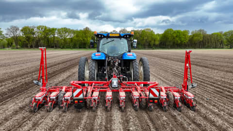 Kverneland Monopill 12r iXtra Life precision seeder attached to a blue tractor, planting evenly spaced rows in a freshly tilled field, optimized for sugar beet, maize, and vegetable seeding with high accuracy and durability.