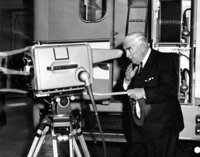 Prime Minister Robert Menzies peers into a new telecine camera for television station ADS7 at Philips Electrical Industries Factory in Adelaide, South Australia, 21 September 1959