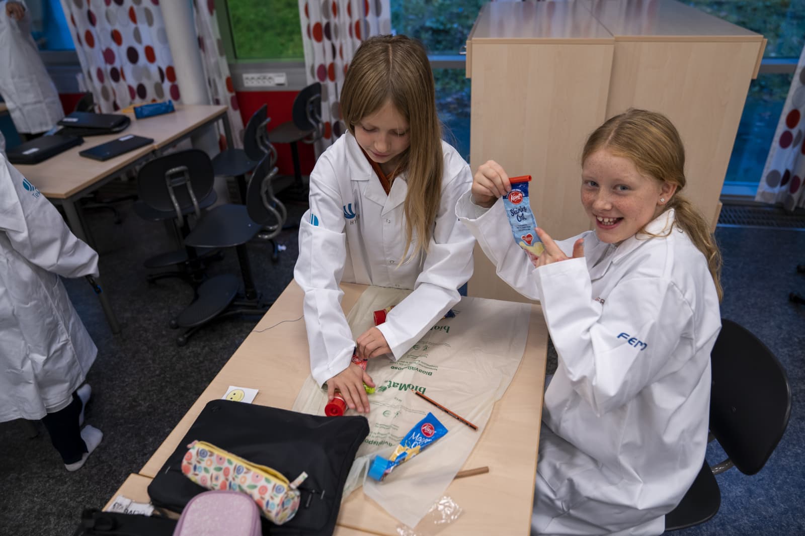 Hvordan tømmer man tuben for mest mulig smøreost før resirkulering? Det tester disse to jentene i forskerfrakker, ved hjelp av verktøy som tubeklemmer og blyanter. Nevene kommer også til god nytte.
