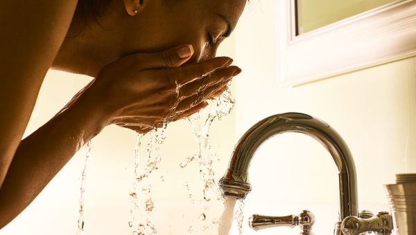 woman washing her face, water dripping into sink