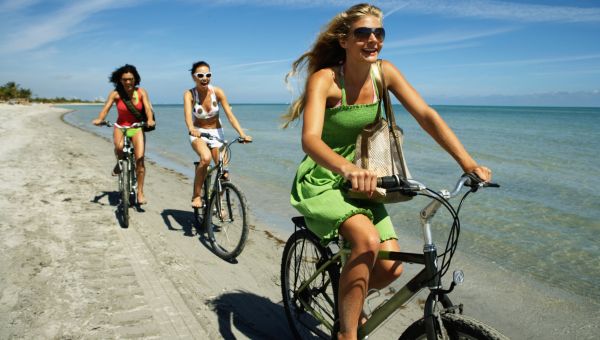 Three young women riding bicycles on beach, smiling