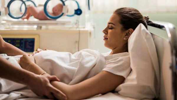 woman, hospital, after childbirth, baby in the background