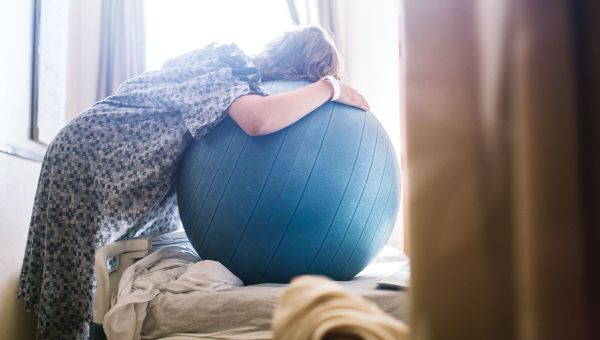 woman leaning on exercise ball, hospital room, hospital gown, pregnant woman