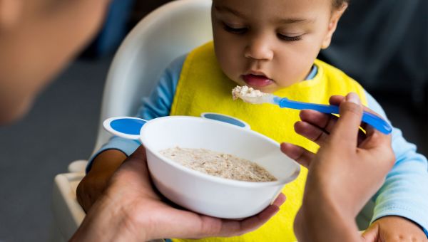 Mother feeding baby spoonfuls of oatmeal or porridge