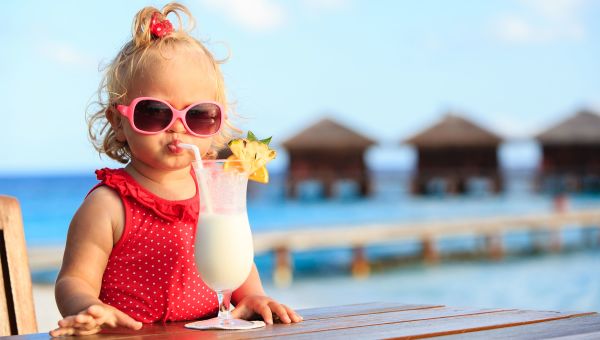 Toddler girl sitting beachside and sipping a milkshake