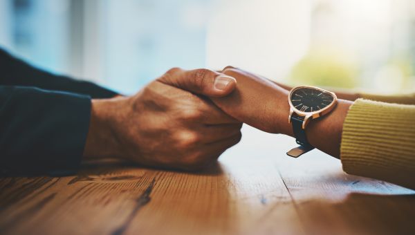 A couple sitting at a table holds hands, providing one another with emotional support.