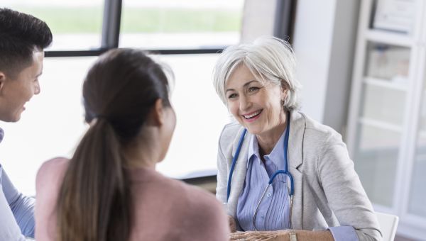 older woman doctor talking to young couple