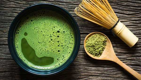 Matcha tea in a mug with a scoop of matcha sitting right next to it.