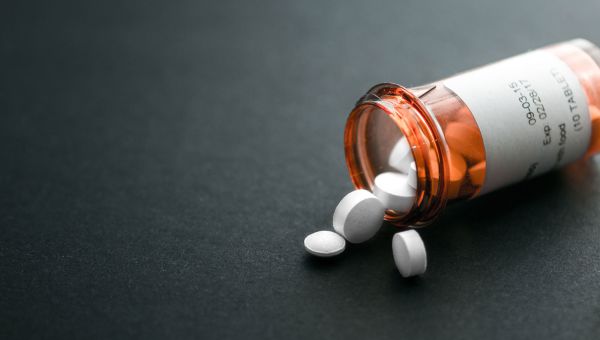 Open pill bottle with pills spilling on to table.