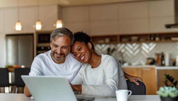 mixed-race middle aged couple sit happily at computer