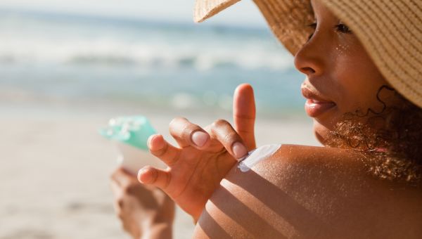 woman in hat reapplying sunscreen at beach