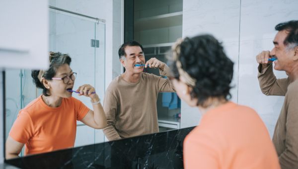 mature asian couple brushing teeth together in bathroom mirror