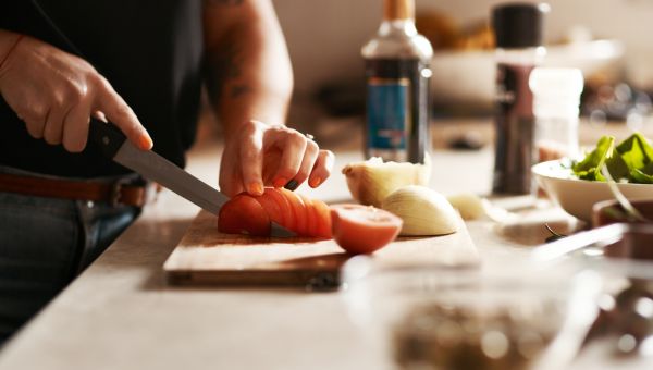 Close up of the hands of a person chopping tomatoes with other types vegetables on the countertop nearby