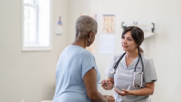 a nurse in gray scrubs speaks with an older Black woman about her condition