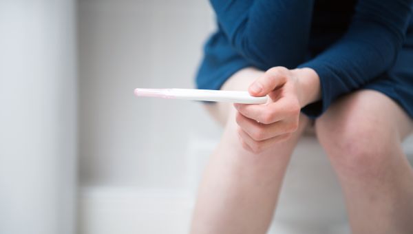 Lower legs of someone sitting on a toilet and holding a home pregnancy test