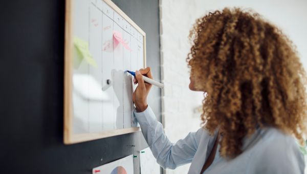 a Black woman writes with a dry erase marker on a scheduling board