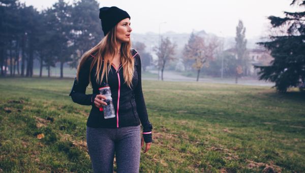 a middle aged white woman in workout clothing walks across a grassy hill on a cloudy day