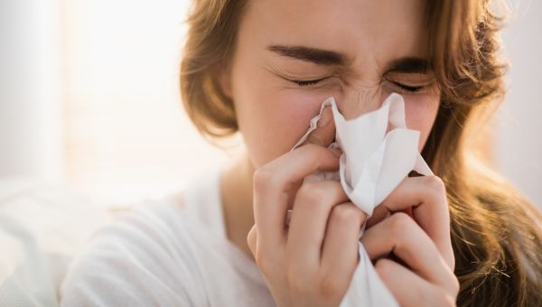 young woman blowing nose sneezing indoors