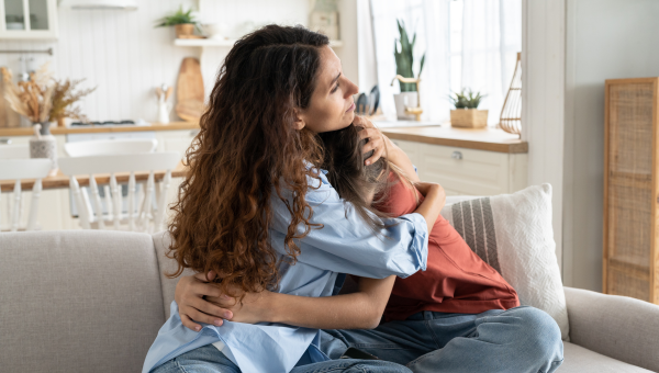 Mother and daughter with ADHD sit facing each other on the couch hugging, heads buried in each other